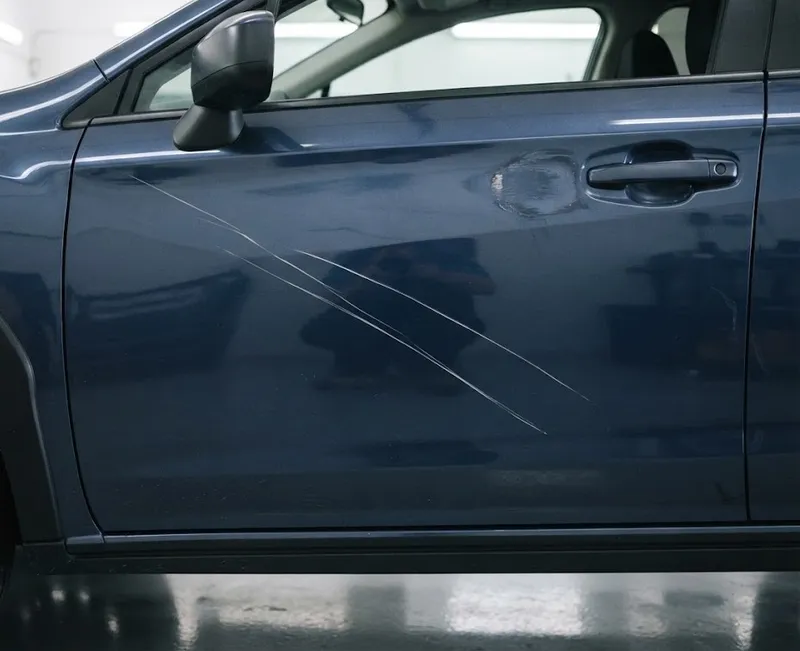 Grande plano da porta azul-escura de um carro com riscos compridos na pintura